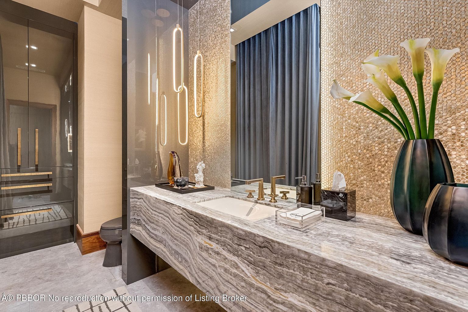 This is a stylish guest bathroom featuring a unique marble countertop with an integrated sink and gold-toned fixtures. The walls are adorned with a mosaic tile pattern, and modern pendant lights hang above the vanity. A dark cabinet provides storage, and a vase of white calla lilies adds a touch of elegance.