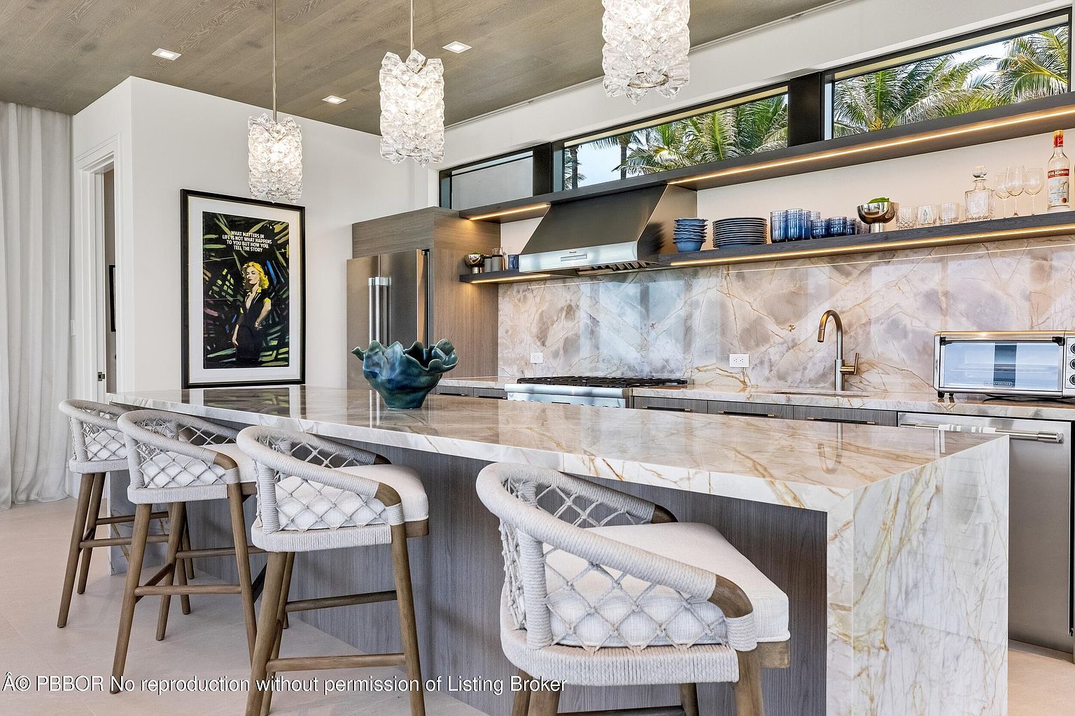 This interior shot showcases a modern kitchen with a luxurious marble countertop island and backsplash. The kitchen features stainless steel appliances, open shelving with decorative items, and stylish pendant lighting. Bar stools line the island, creating an inviting space for dining and socializing.