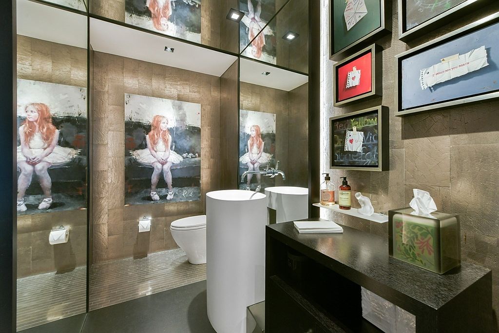 This sophisticated powder room features a striking, artistic aesthetic with a large, moody portrait of a girl in a white dress serving as a focal point. The space is defined by textured metallic wall tiles, a sleek cylindrical pedestal sink, and a dark wood vanity, all reflected in expansive mirrored panels that enhance the room's depth. The overall impression is one of high-end, contemporary luxury with a unique, gallery-like atmosphere.