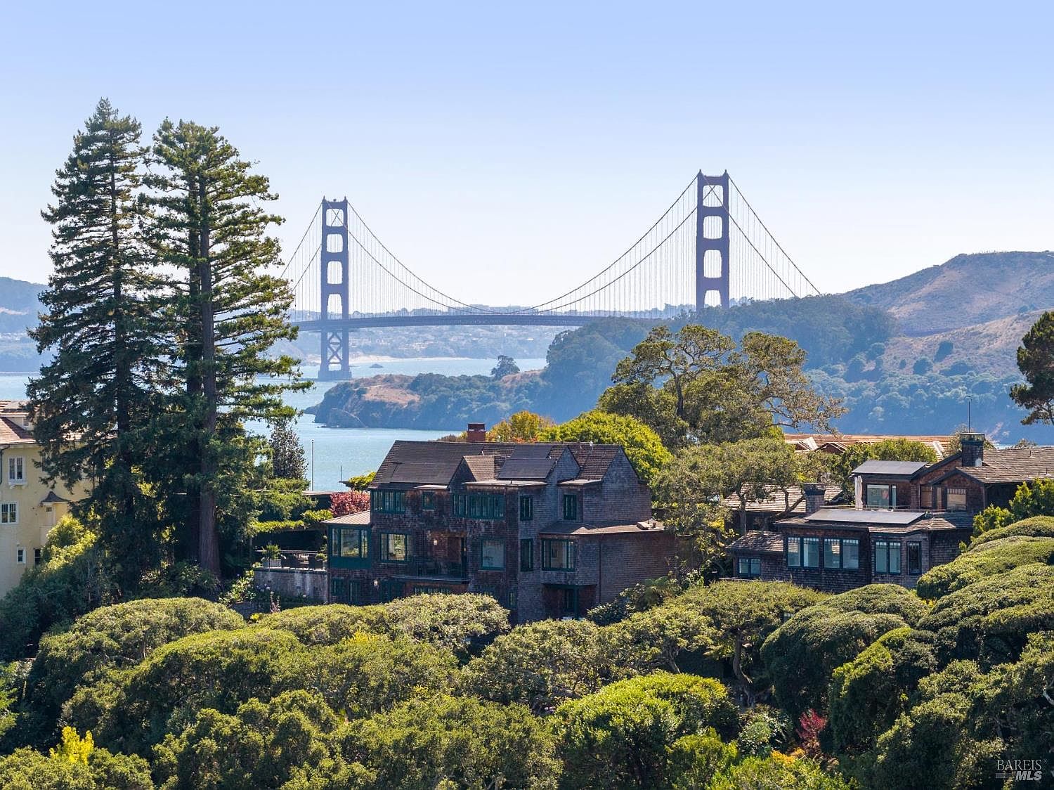 This image showcases a beautiful home with a view of the Golden Gate Bridge. The house is surrounded by lush greenery, creating a sense of privacy and tranquility. The architectural style appears to be traditional, with a focus on natural materials and a harmonious integration with the landscape.
