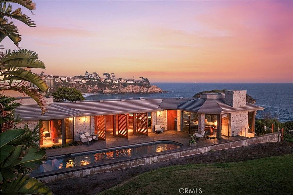 This image showcases a luxurious home with an inviting pool and spa area overlooking the ocean at sunset. The architectural style is modern with stone accents and large windows, creating a seamless indoor-outdoor living experience. The property exudes elegance and tranquility, perfect for a high-end real estate listing.