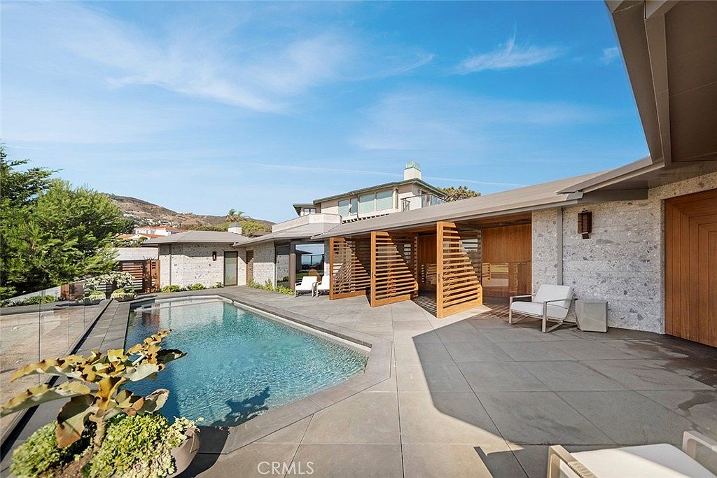 This image showcases a luxurious backyard featuring a modern pool and spa area. The pool is surrounded by a sleek patio with contemporary outdoor furniture and a unique wooden structure providing shade and architectural interest. The overall impression is one of sophisticated outdoor living and relaxation.
