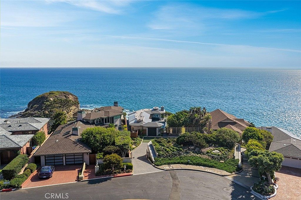 This aerial shot showcases a collection of luxury homes nestled along the coastline, offering stunning ocean views. The properties feature well-manicured landscaping, private driveways, and architectural designs that complement the coastal setting. The image captures the exclusivity and serene atmosphere of this high-end residential area.