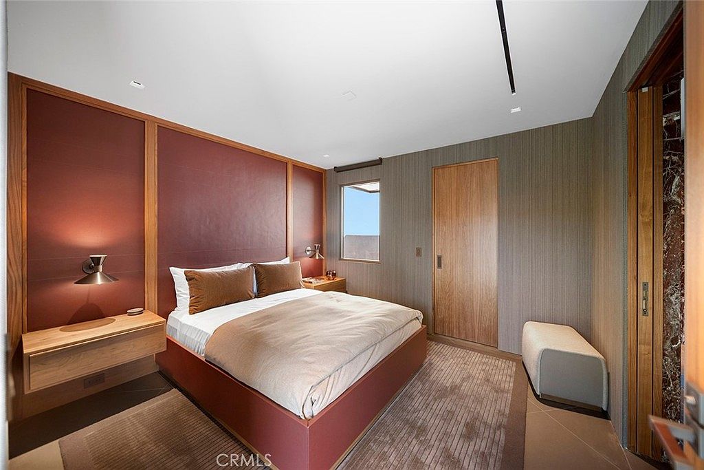 This is a primary bedroom featuring a large bed with a brown headboard and matching pillows. The room has a modern design with a minimalist aesthetic, including a floating nightstand and a small window providing natural light. The color palette is warm and inviting, creating a comfortable and stylish space.