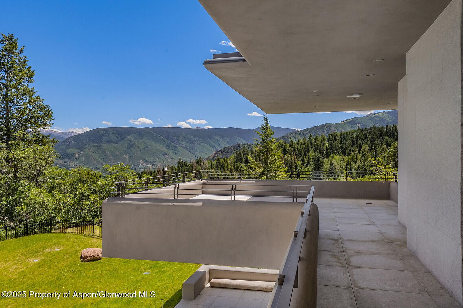 This image showcases a modern balcony with a stunning mountain view. The balcony features a sleek, minimalist design with concrete walls and metal railings. The foreground includes a well-maintained lawn and a glimpse of the surrounding landscape, creating a sense of tranquility and luxury.