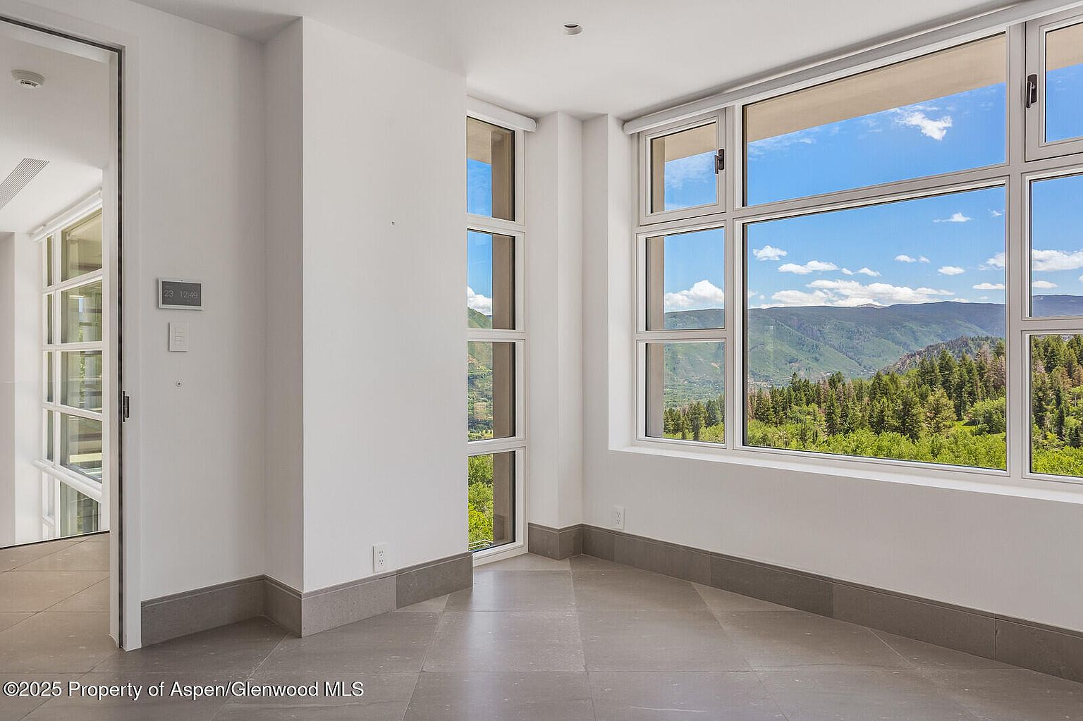 This interior shot showcases a bright hallway with large windows offering scenic mountain views. The room features neutral-toned walls, gray flooring, and modern architectural details. The space is well-lit and appears spacious, creating a welcoming and airy atmosphere.