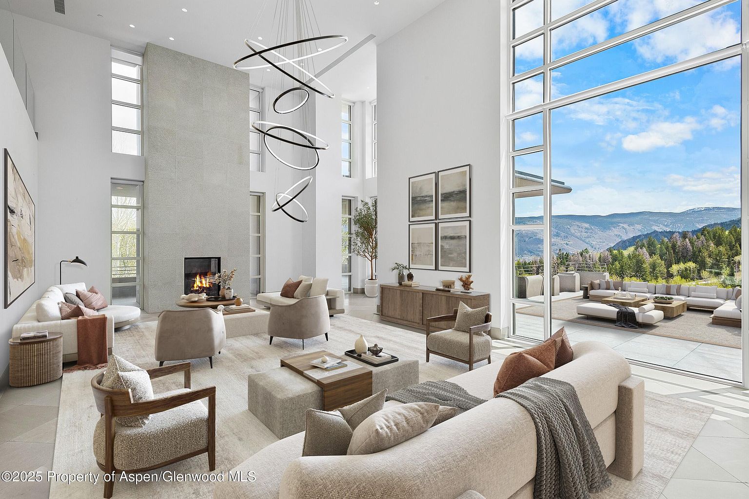 This is a spacious and luxurious living room featuring high ceilings, a modern fireplace, and large windows offering stunning mountain views. The room is furnished with comfortable seating arrangements, including sofas and armchairs, arranged around a central coffee table. The overall design is contemporary and elegant, creating a welcoming and sophisticated atmosphere.