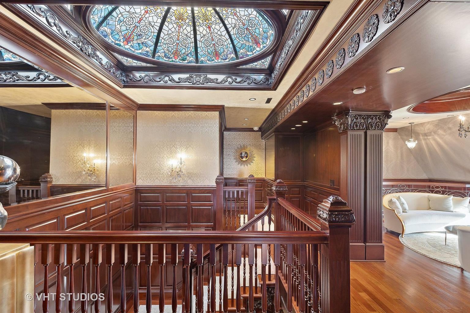 This interior shot showcases an elegant hallway and staircase featuring rich, dark wood paneling and intricate architectural details. A stained glass dome skylight illuminates the space, adding a touch of luxury. The overall impression is one of classic sophistication and grandeur, highlighting the home's high-end craftsmanship.