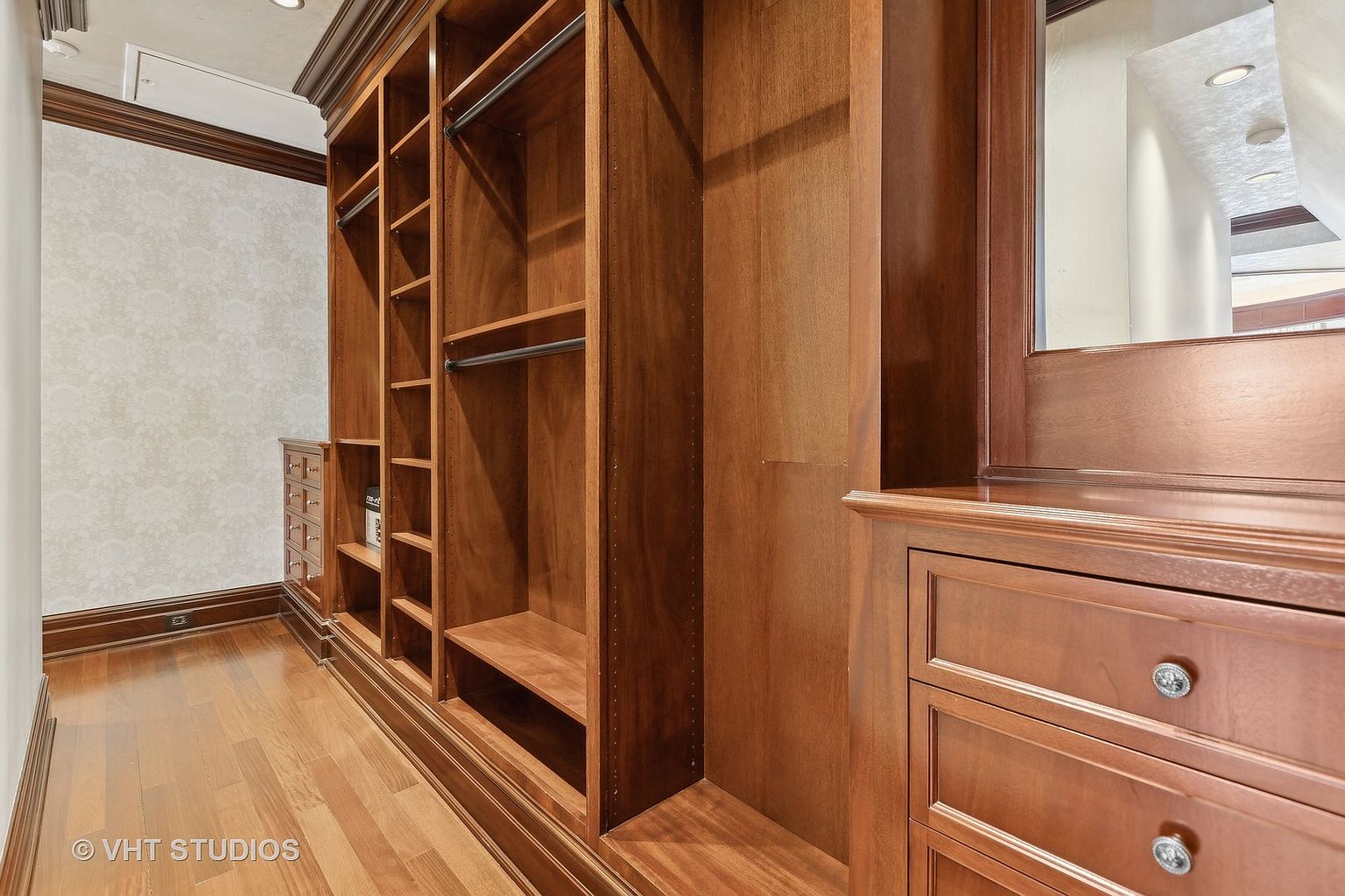 This is a well-organized walk-in closet featuring custom wood cabinetry with shelving, drawers, and hanging rods. The warm wood tones and ample storage space create a luxurious and functional area. The closet is well-lit and appears spacious, offering a desirable feature for potential buyers.