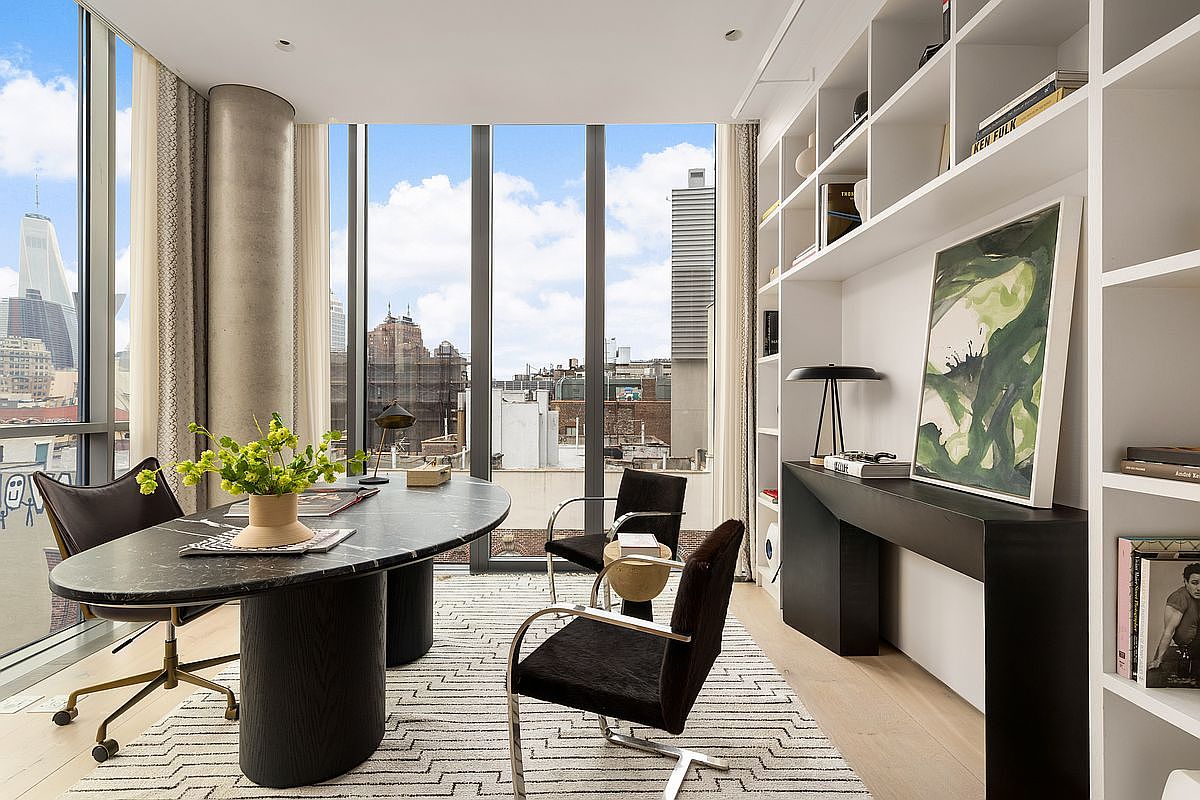This sophisticated home office features a striking oval-shaped desk with a dark stone top and cylindrical base, positioned to take advantage of the expansive floor-to-ceiling windows that offer a panoramic city view. The room is anchored by a geometric patterned area rug and includes built-in white shelving units that frame a sleek black console table topped with a piece of abstract art. The space exudes a modern, professional aesthetic with a clean color palette and high-end finishes.
