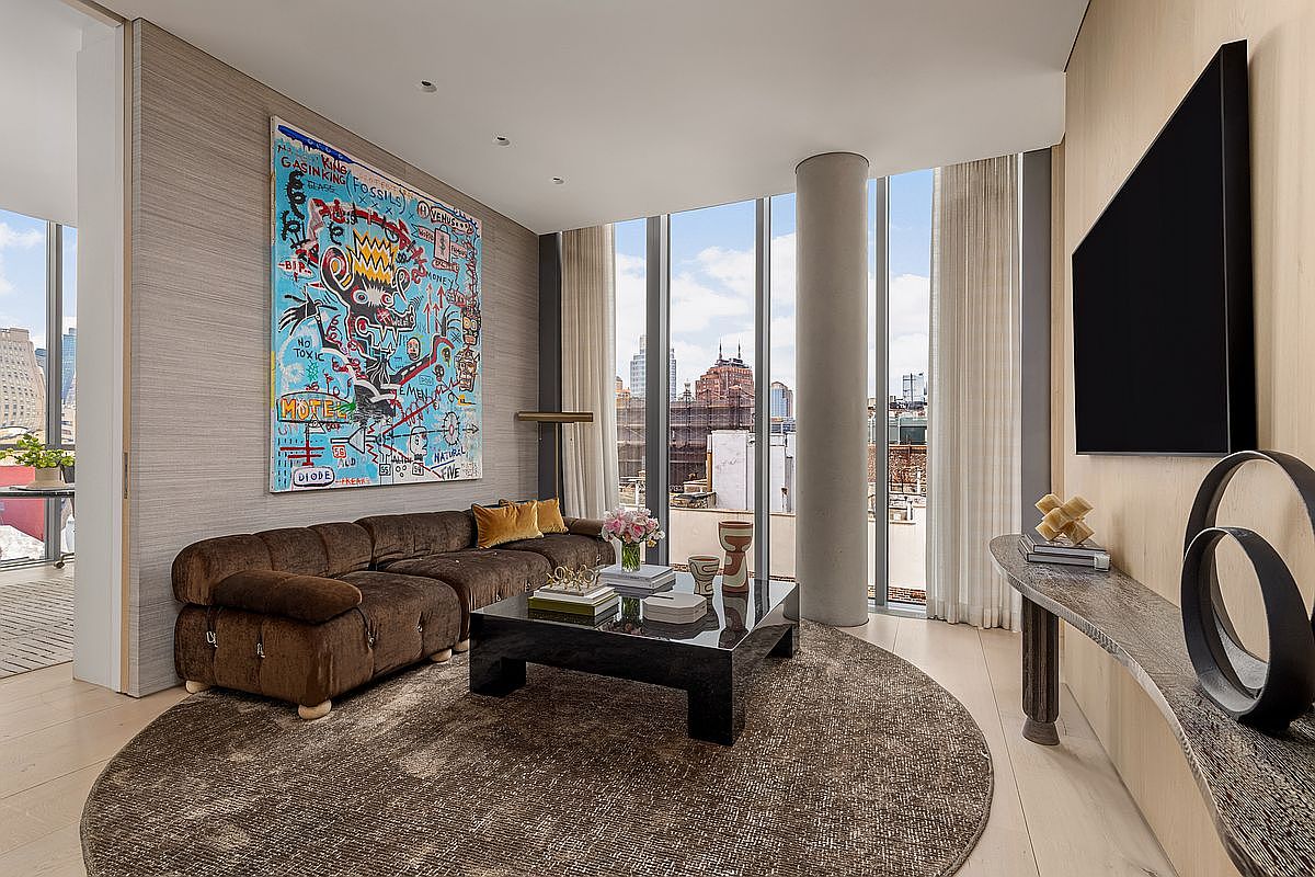 This sophisticated living room features a plush, brown velvet sofa accented with gold pillows, positioned around a sleek, dark-toned coffee table on a large circular area rug. A vibrant, abstract art piece serves as a bold focal point on the textured wall, while floor-to-ceiling windows provide expansive city views and abundant natural light. The space is completed by a minimalist console table beneath a wall-mounted television, creating a modern and curated atmosphere.