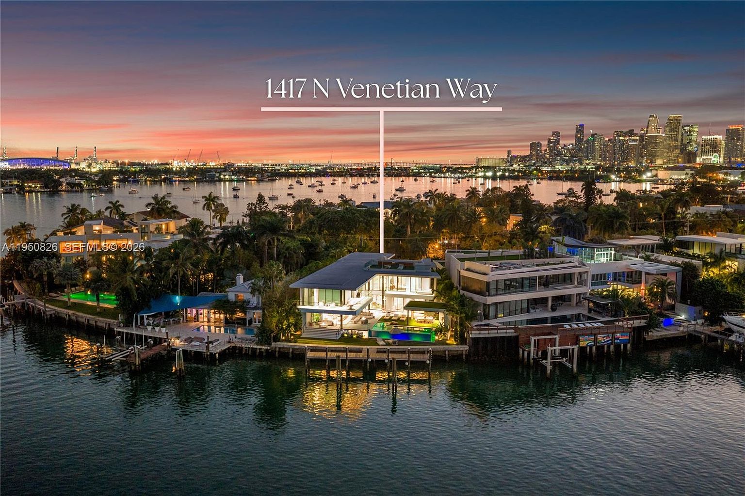 This aerial view showcases a luxurious waterfront property at dusk, featuring modern architectural design with expansive glass walls and a private pool. The property is surrounded by lush greenery and offers stunning views of the city skyline across the water. The overall impression is one of high-end living and sophisticated style.