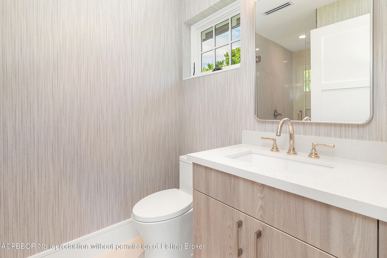 This is a well-lit guest bathroom featuring a modern vanity with a white countertop and light wood cabinetry. A rectangular mirror hangs above the sink, reflecting a glimpse into the shower area. The walls are covered in a subtle striped wallpaper, and a small window provides natural light.