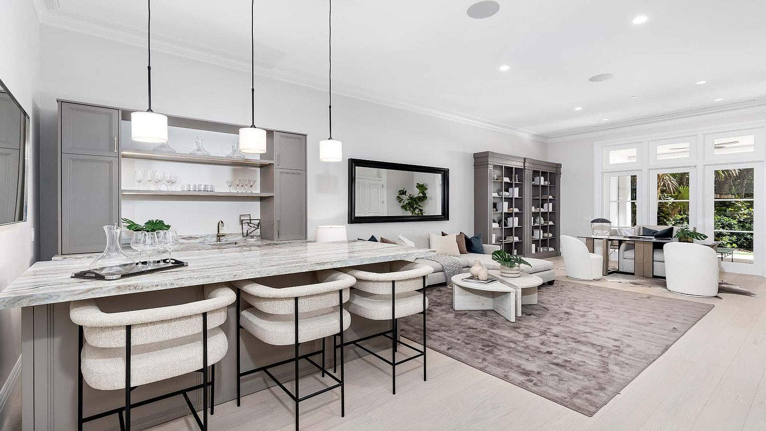 This interior shot showcases a stylish living room with a bar area. The space features a gray color palette, with a marble countertop bar, comfortable seating, and built-in bookshelves. Large windows provide natural light, enhancing the room's inviting atmosphere.