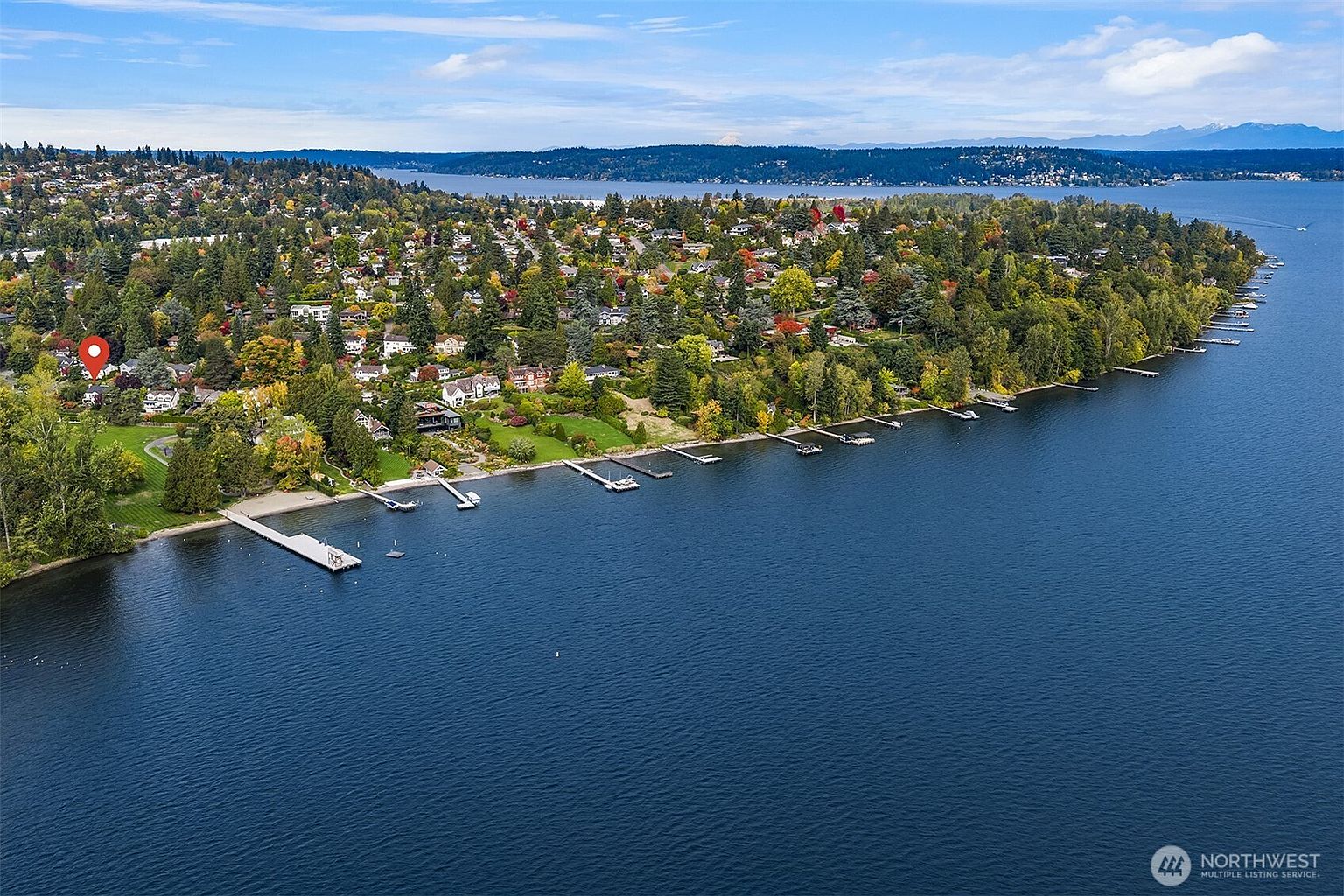 This aerial view showcases a stunning waterfront property with lush greenery and a series of private docks extending into the calm, blue water. The landscape features a mix of mature trees and well-maintained lawns, dotted with residential homes. The overall impression is one of tranquility and exclusivity, highlighting the property's prime location and access to the water.