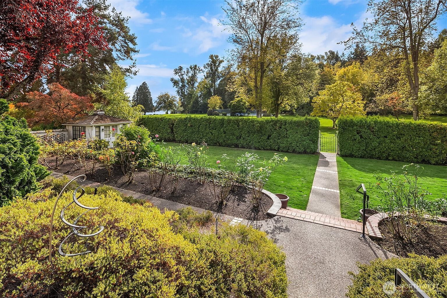 This image showcases a meticulously maintained garden with lush green lawns, manicured hedges, and vibrant flower beds. A charming garden path leads through an arched gate, inviting exploration of the serene outdoor space. The overall impression is one of tranquility and refined landscaping, perfect for relaxation and outdoor enjoyment.