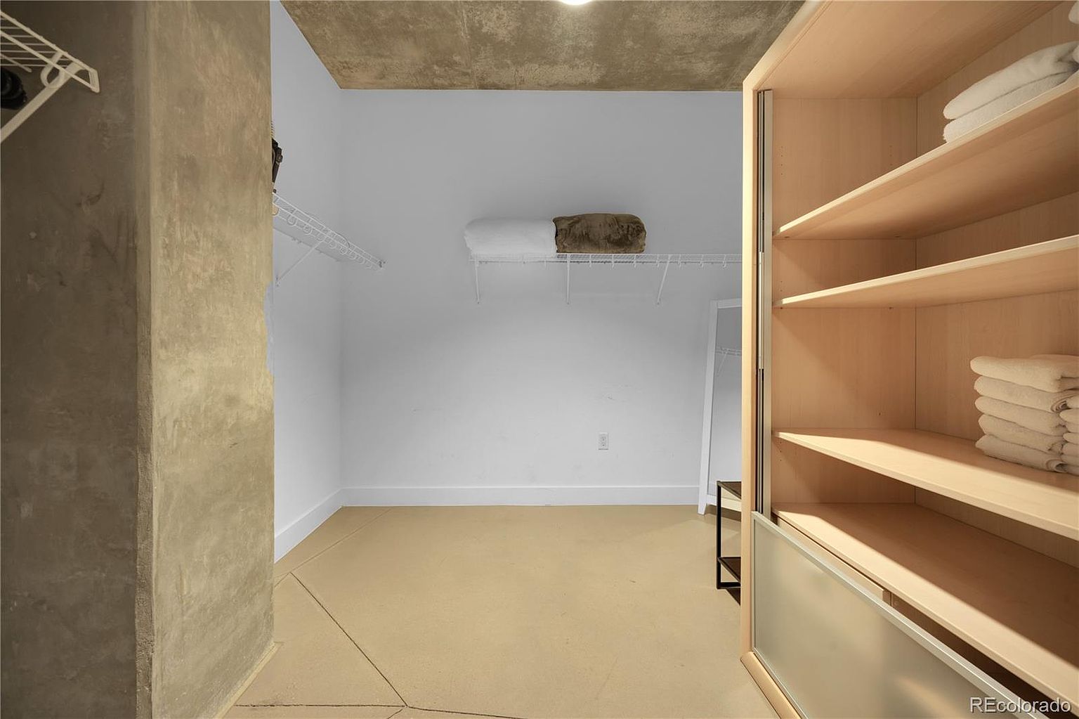 This image showcases a well-organized walk-in closet. It features built-in shelving with neatly stacked towels, a wire shelf with folded blankets, and ample open space. The closet has a neutral color palette and a clean, minimalist design, suggesting a functional and tidy storage solution.