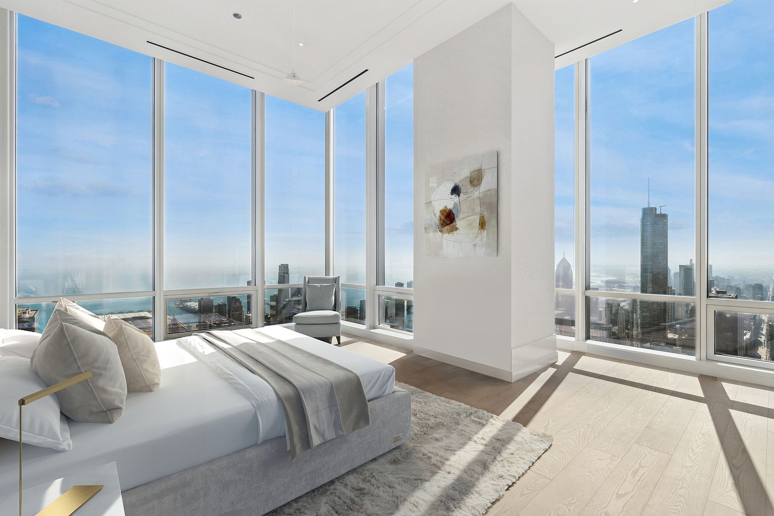 This is a luxurious primary bedroom featuring floor-to-ceiling windows with stunning city views. The room is furnished with a plush bed, a stylish chair, and modern artwork. The light wood flooring and neutral color palette create a serene and sophisticated atmosphere, perfect for relaxation.