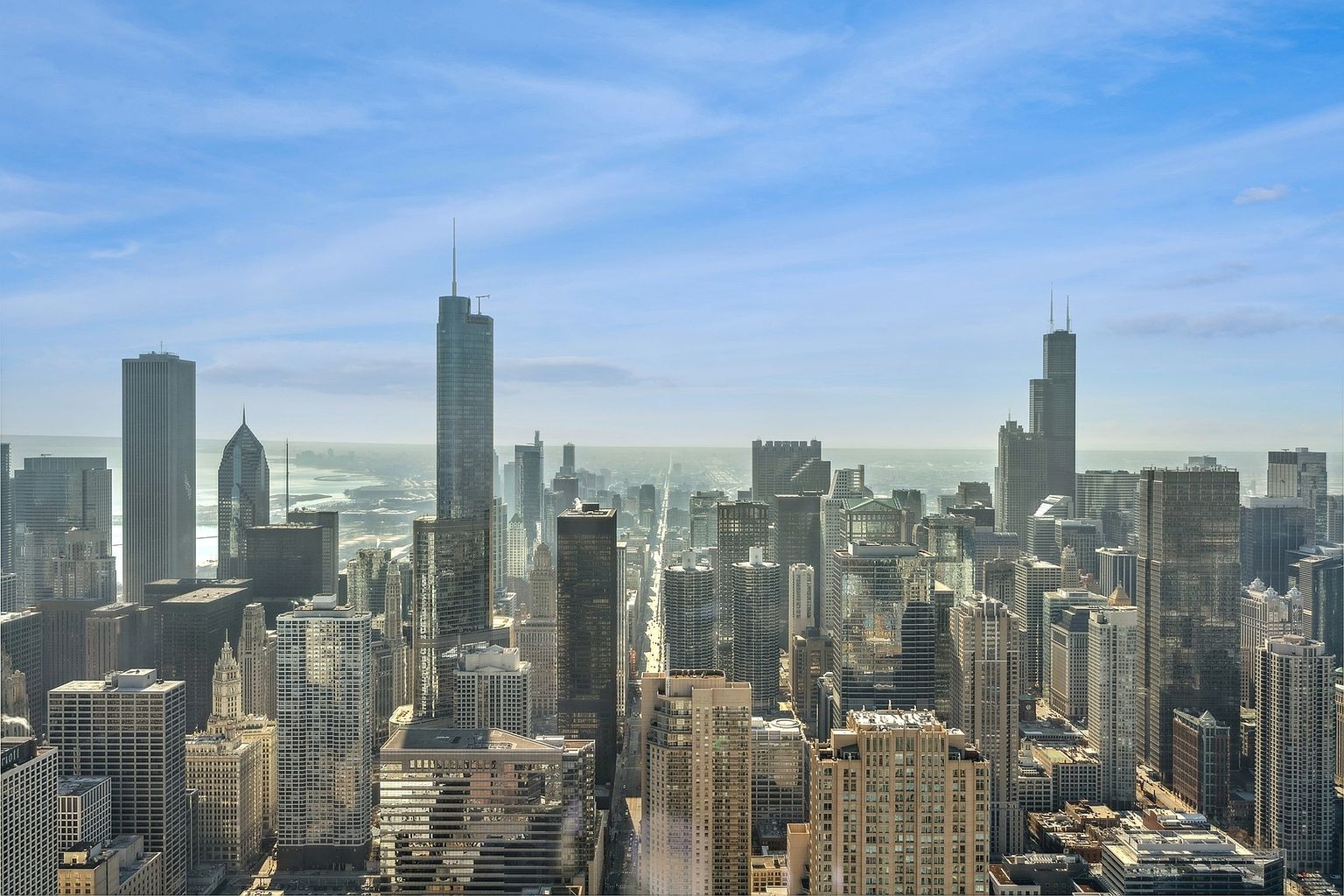 This aerial view showcases a dense cityscape with numerous skyscrapers under a bright, partly cloudy sky. The buildings vary in height and architectural style, creating a dynamic urban landscape. The image conveys a sense of scale and the vibrant energy of a major metropolitan area, perfect for highlighting the location of a property.