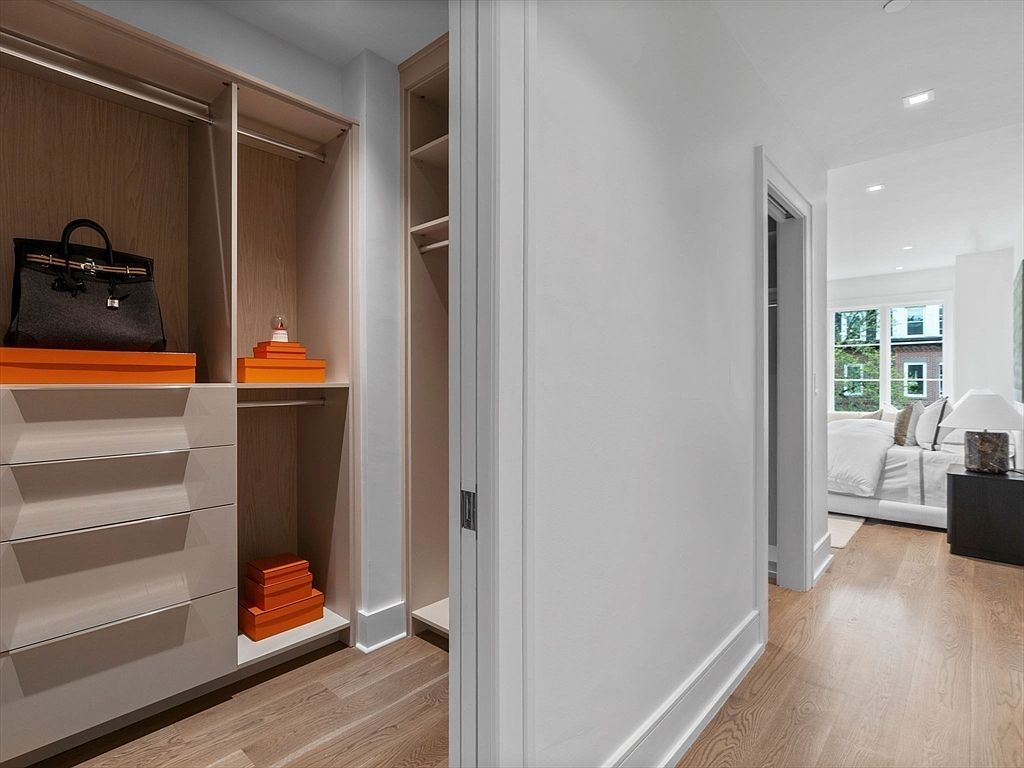 This image showcases a well-organized walk-in closet with custom shelving and drawers. A black handbag sits atop an orange box, adding a pop of color. The closet is adjacent to a hallway leading into a bedroom, creating a seamless transition between spaces.
