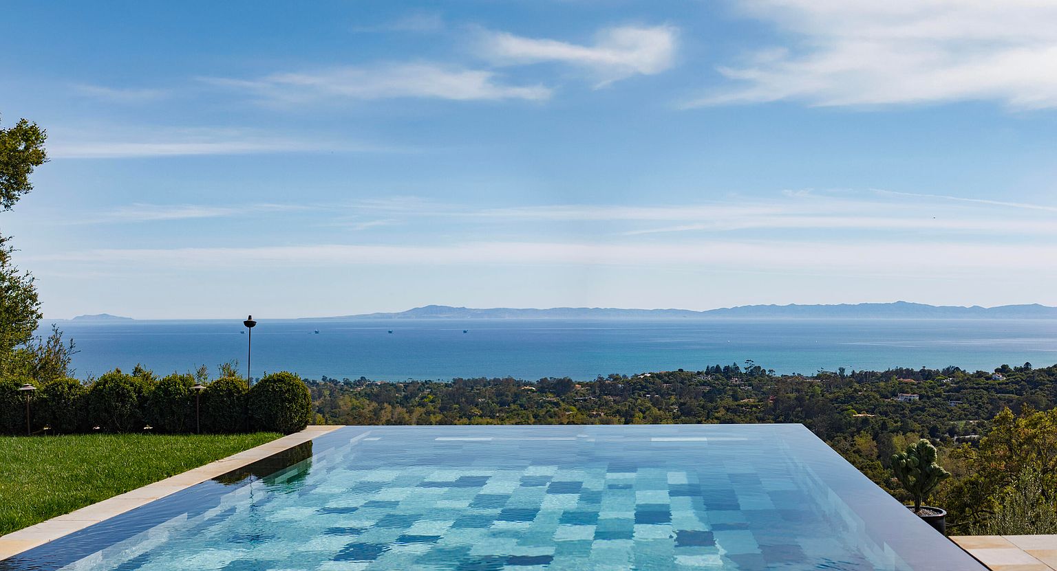 This image showcases a luxurious infinity pool with a stunning ocean view. The pool's tile design adds a touch of elegance, while the surrounding landscape features lush greenery and manicured lawns. The scene evokes a sense of tranquility and high-end living, perfect for attracting discerning buyers.