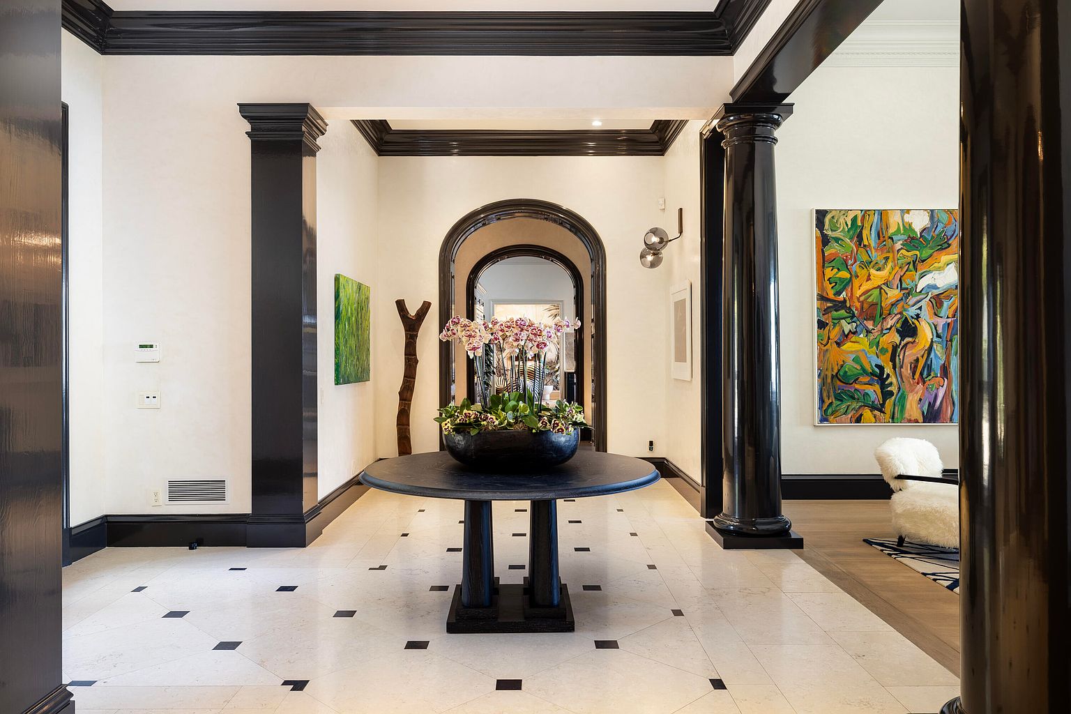 This interior shot showcases a grand hallway with a striking black and white color scheme. The glossy black trim and columns contrast with the light-colored walls and tiled floor, creating a sophisticated and modern aesthetic. A round table with a floral arrangement serves as a focal point, while arched doorways lead to other areas of the home, enhancing the sense of depth and luxury.