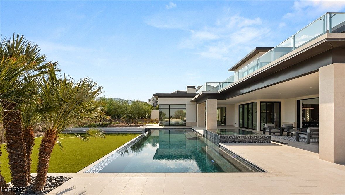 This image showcases a luxurious backyard featuring a modern home with a stunning pool and spa area. The pool's sleek design complements the contemporary architecture of the house, which includes a covered patio with outdoor seating. Lush landscaping and a well-manicured lawn add to the property's appeal, creating an inviting and relaxing outdoor space.