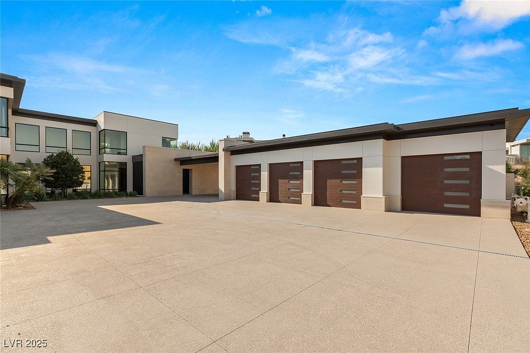 This image showcases the exterior of a modern home, focusing on the garage area. The garage features multiple bays with sleek, contemporary doors, complemented by a spacious concrete driveway. The architectural style is clean and minimalist, with a focus on horizontal lines and a neutral color palette.