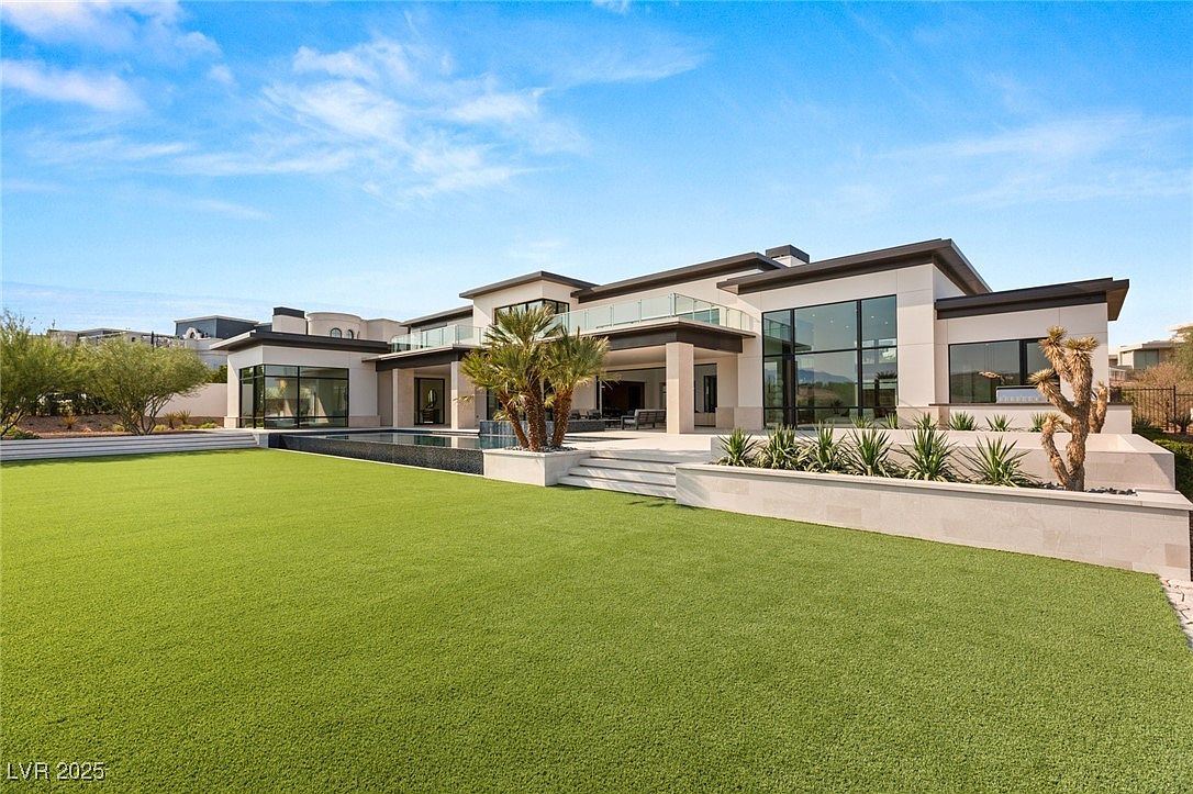 This image showcases the rear exterior of a modern luxury home, featuring a well-manicured lawn, a sleek pool, and multiple outdoor living spaces. The architecture emphasizes clean lines, large windows, and balconies, creating a seamless transition between indoor and outdoor living. The overall impression is one of sophistication and upscale comfort.