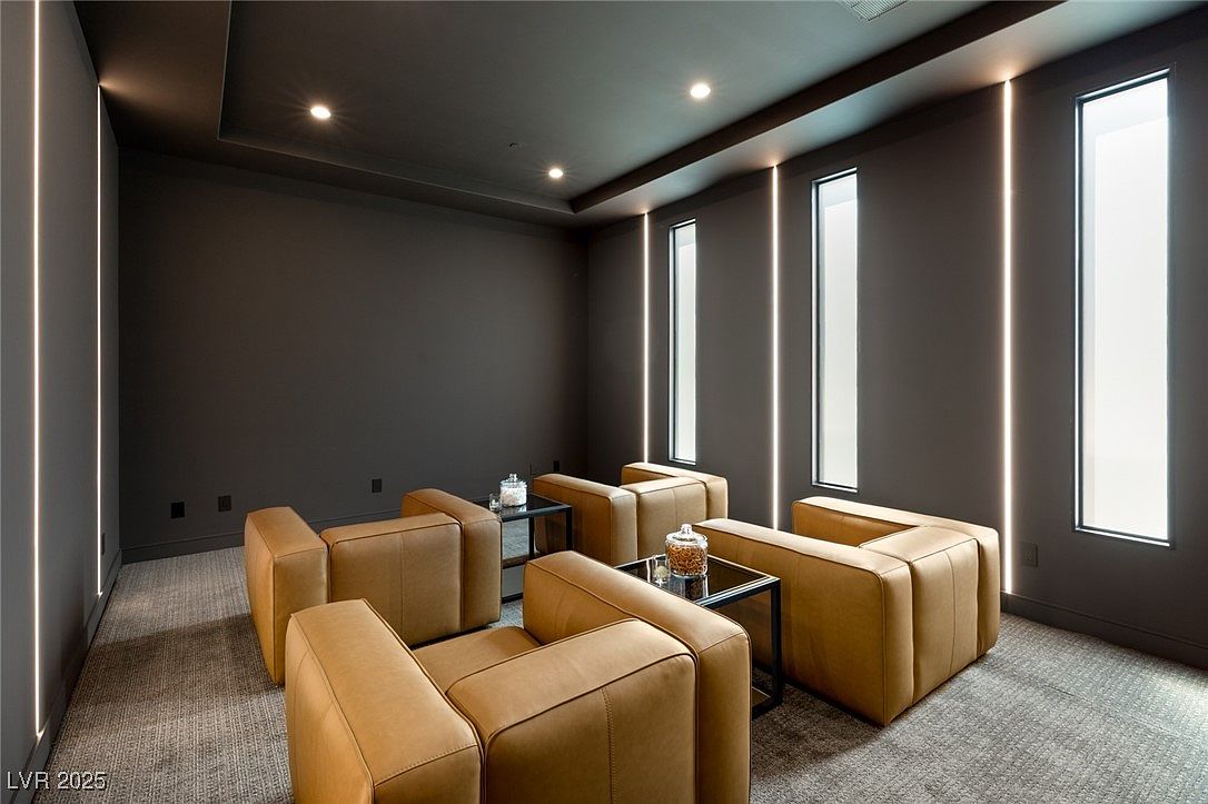 This interior shot showcases a modern living room with a sophisticated color palette. The room features four tan leather armchairs arranged around two small black tables, creating an intimate seating area. Vertical LED light strips add a contemporary touch, complementing the dark walls and ceiling, while small windows provide natural light.