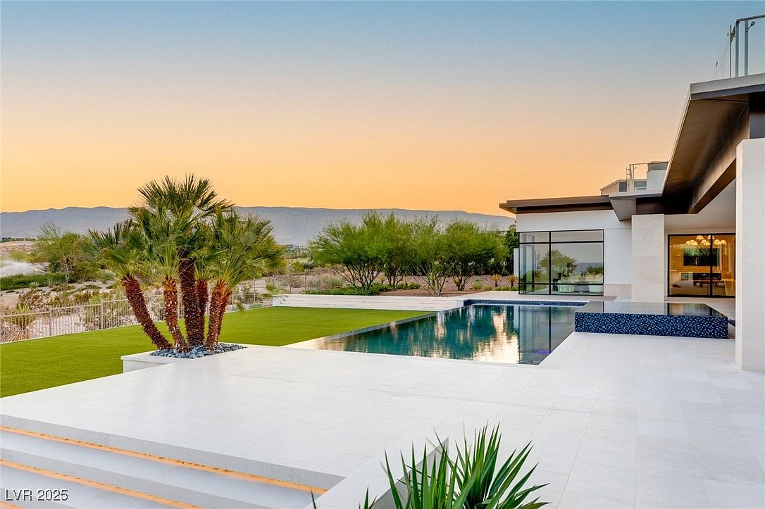 This image showcases a luxurious backyard featuring a modern home with a stunning pool and spa area. The pool's sleek design complements the contemporary architecture of the house, while the surrounding landscaping adds a touch of natural beauty. The white tiled patio provides ample space for relaxation and entertainment, making it an ideal outdoor oasis.