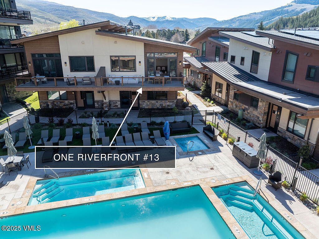 This image showcases an exterior view of a multi-family residential complex, highlighting a pool and spa area. The architecture features a modern design with a combination of stone and wood accents. The pool area includes lounge chairs and umbrellas, creating a relaxing atmosphere, while the surrounding landscape adds to the property's appeal.