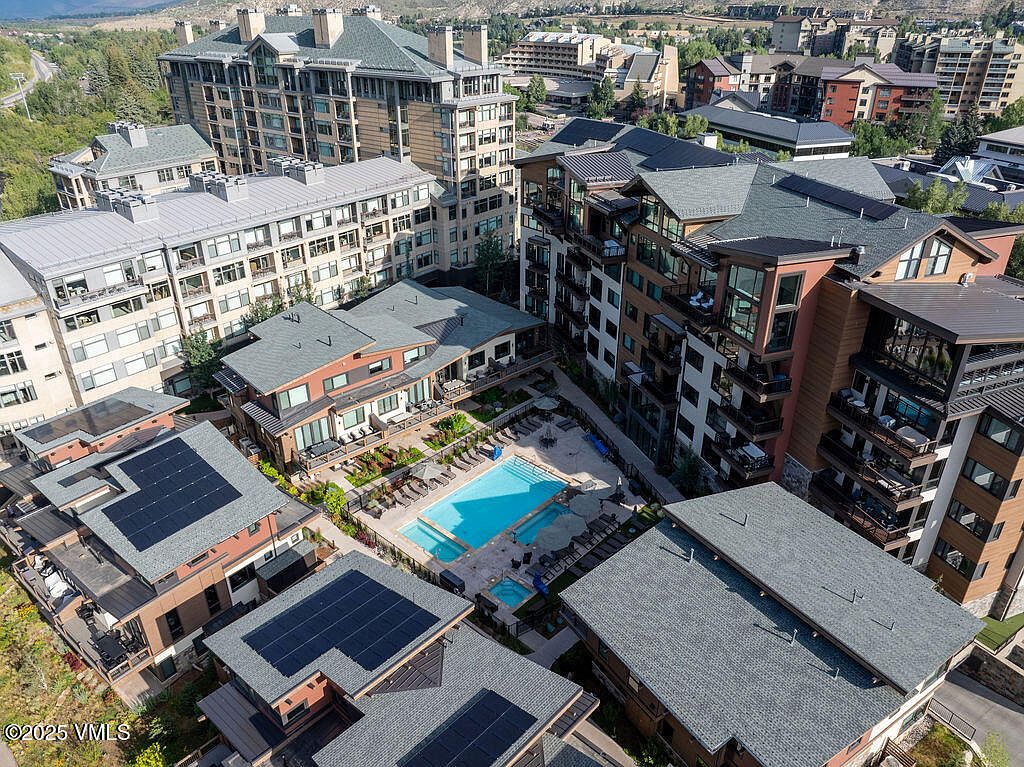 This aerial view showcases a luxurious residential complex with multiple buildings, a central swimming pool, and well-maintained landscaping. The architecture features a mix of modern and traditional elements, with varying rooflines and balcony designs. Solar panels are visible on some of the rooftops, adding an eco-friendly touch to the property.