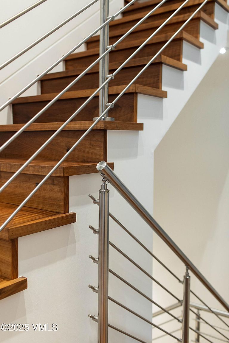 This image showcases a modern staircase with wooden steps and a sleek stainless steel railing system. The design emphasizes clean lines and a minimalist aesthetic, creating a sophisticated and contemporary feel. The white walls provide a neutral backdrop, highlighting the warmth of the wood and the cool tones of the metal.