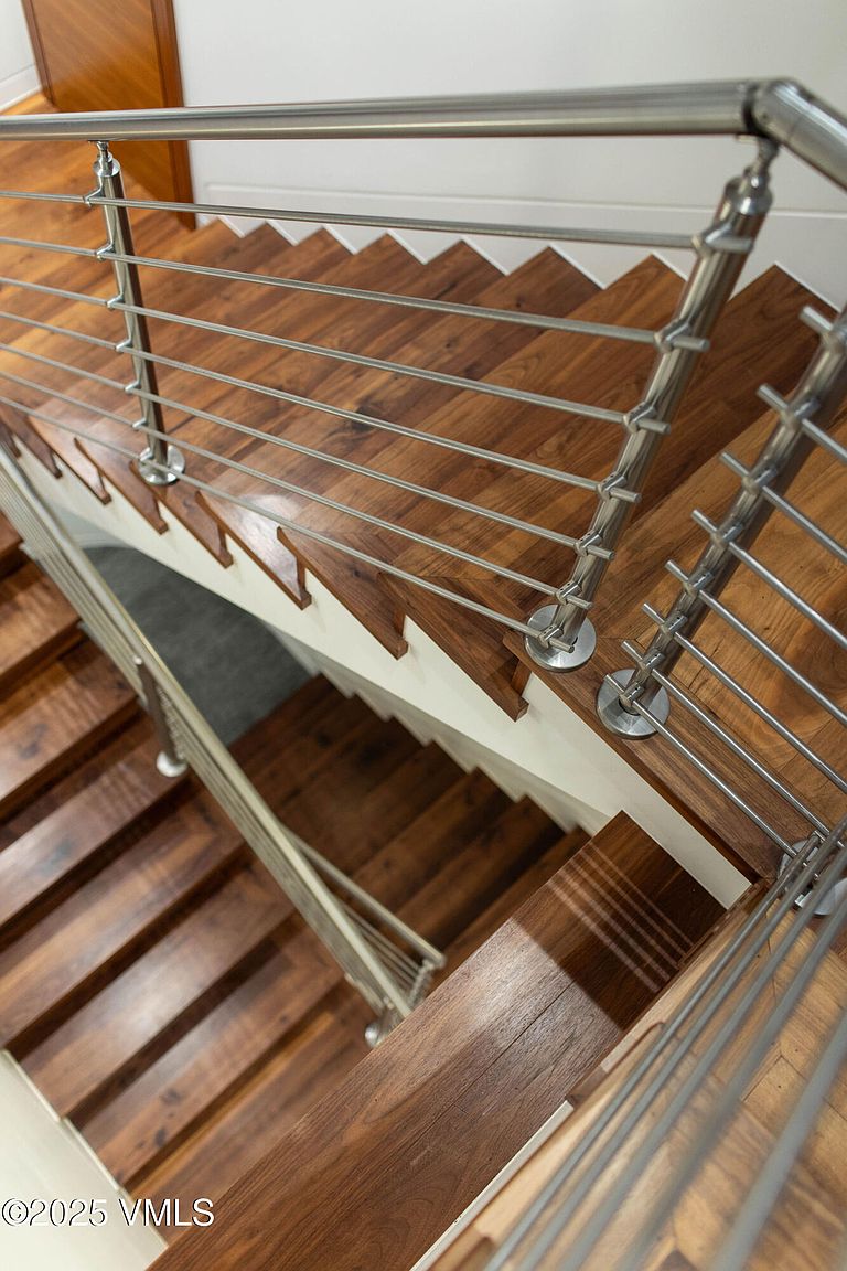 This image showcases a modern staircase with wooden steps and a sleek metal railing system. The steps are a rich, warm wood tone, contrasting with the white risers and the cool metal of the railing. The view is from above, looking down the staircase, emphasizing the clean lines and contemporary design, which would appeal to buyers seeking a stylish and updated home.
