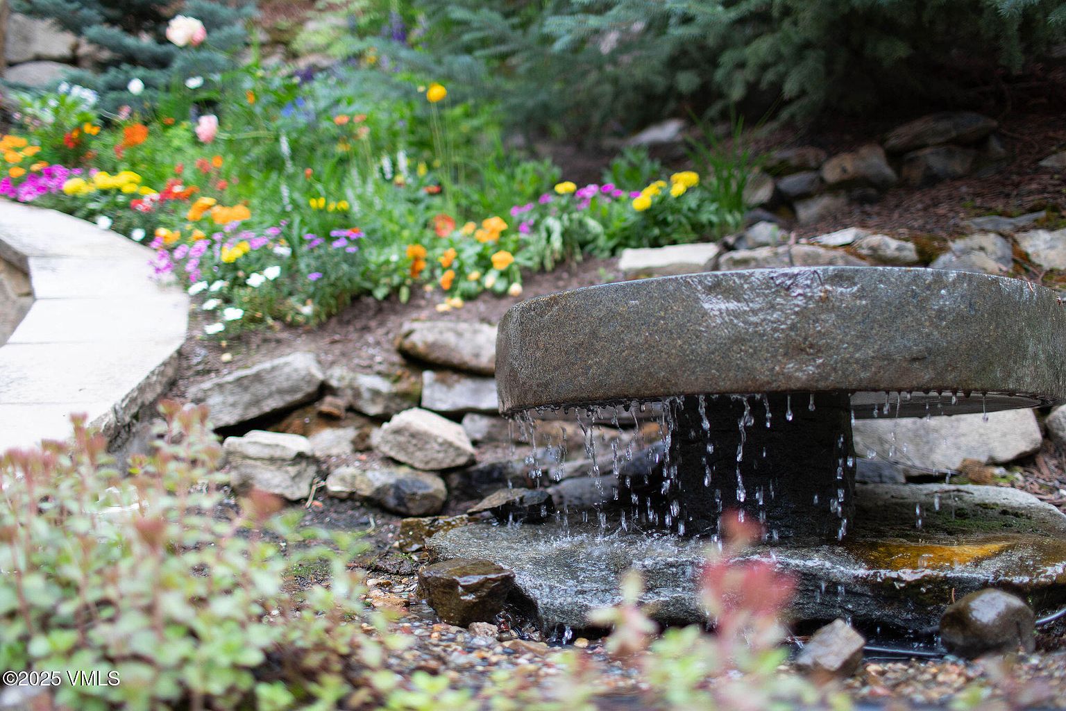This image showcases a beautifully landscaped garden featuring a stone water feature as a focal point. Colorful flowers and lush greenery create a serene and inviting atmosphere. The stone elements add a touch of natural elegance, enhancing the overall appeal of the outdoor space.