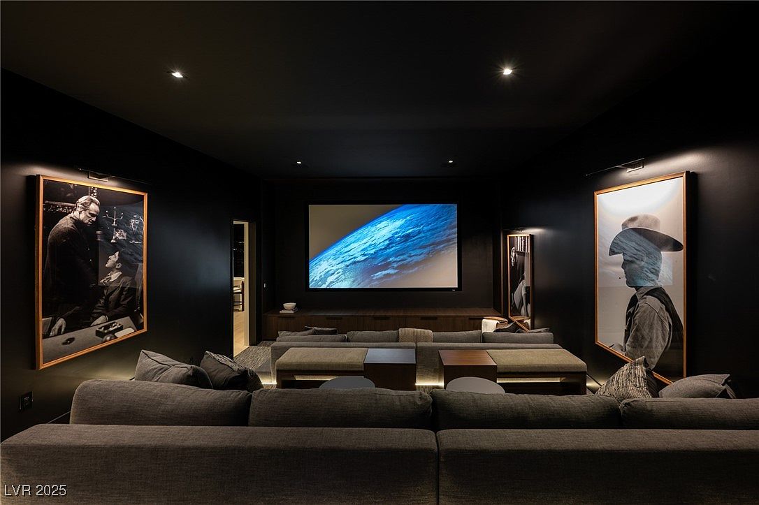 This is a luxurious home theater room featuring a large screen displaying an image of Earth, flanked by framed black and white portraits illuminated by sconces. The room is painted in a dark color, creating an immersive cinematic experience. Comfortable seating is arranged in tiers, providing optimal viewing angles for all occupants.