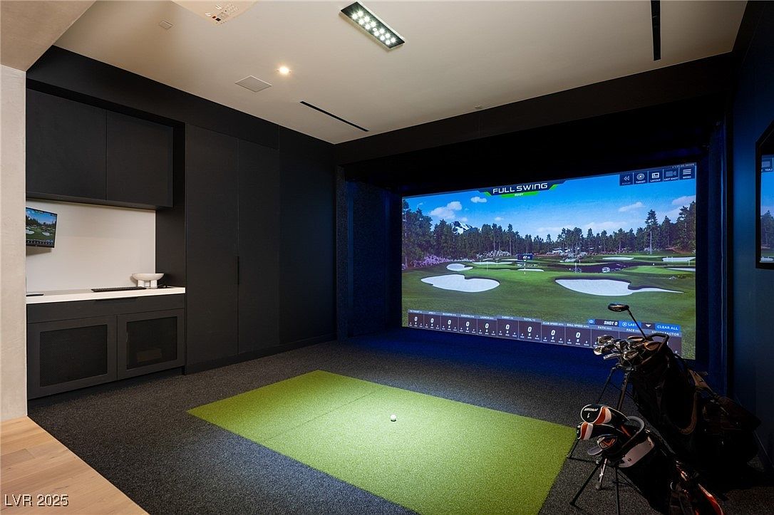 This interior shot showcases a high-end home golf simulator room. The room features a large screen displaying a golf course, a green hitting area, and golf clubs, suggesting a focus on recreation and entertainment. Dark cabinetry and modern lighting contribute to a sophisticated and dedicated space for golf enthusiasts.