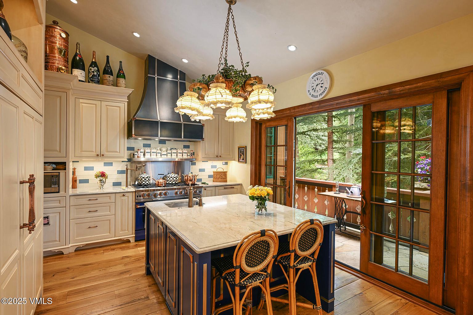 This is a well-appointed kitchen featuring custom cabinetry, a large center island with seating, and high-end appliances. The kitchen has a warm and inviting feel, with natural light streaming in from the adjacent outdoor patio. The design incorporates a mix of traditional and elegant elements, creating a sophisticated culinary space.