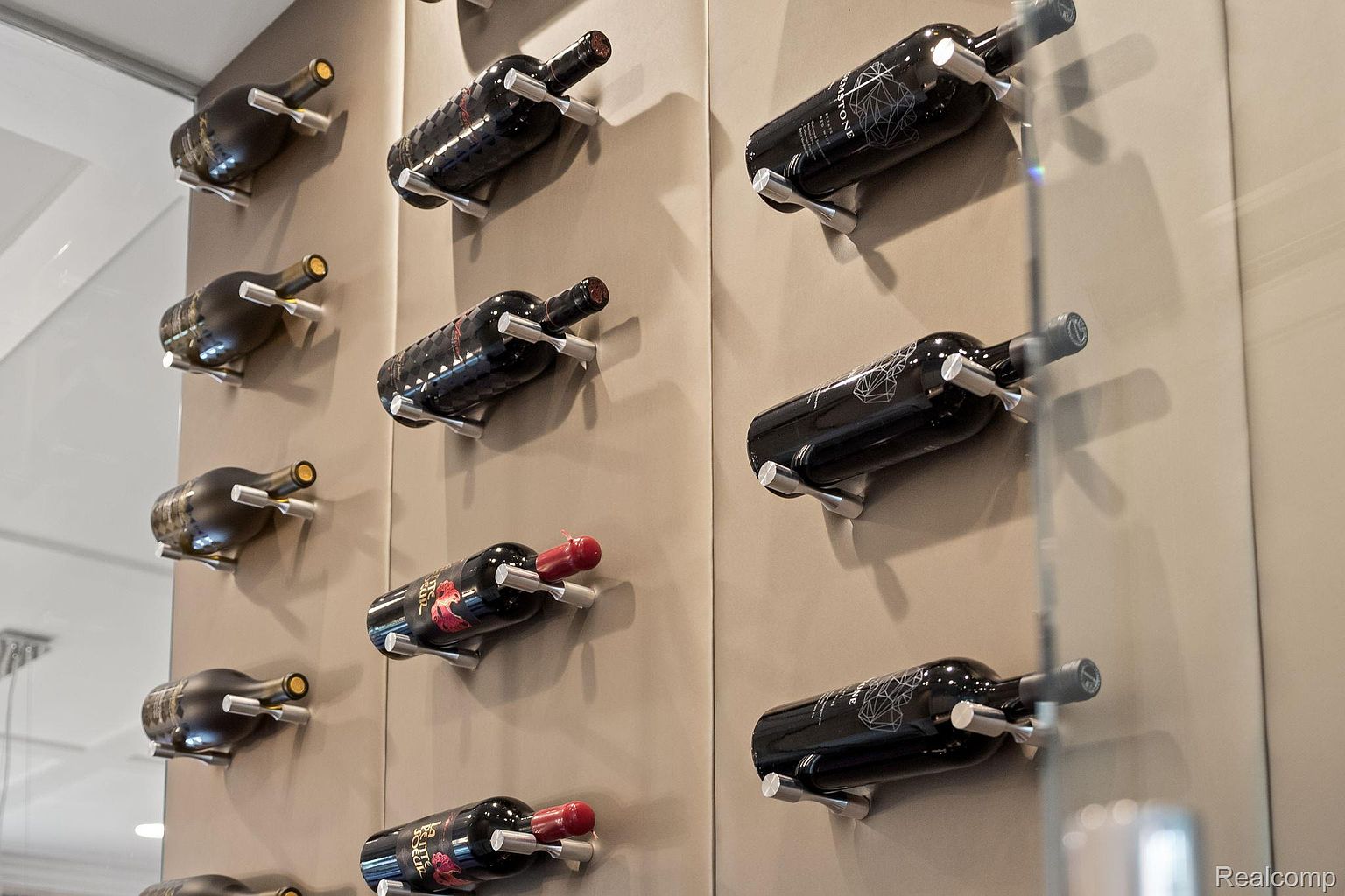 This image showcases a stylish wine display featuring multiple bottles horizontally mounted on a wall with sleek, minimalist silver holders. The bottles are arranged in a grid pattern, creating a visually appealing and organized presentation. The wall has a neutral tone, which complements the dark colors of the wine bottles, adding a touch of sophistication to the space.