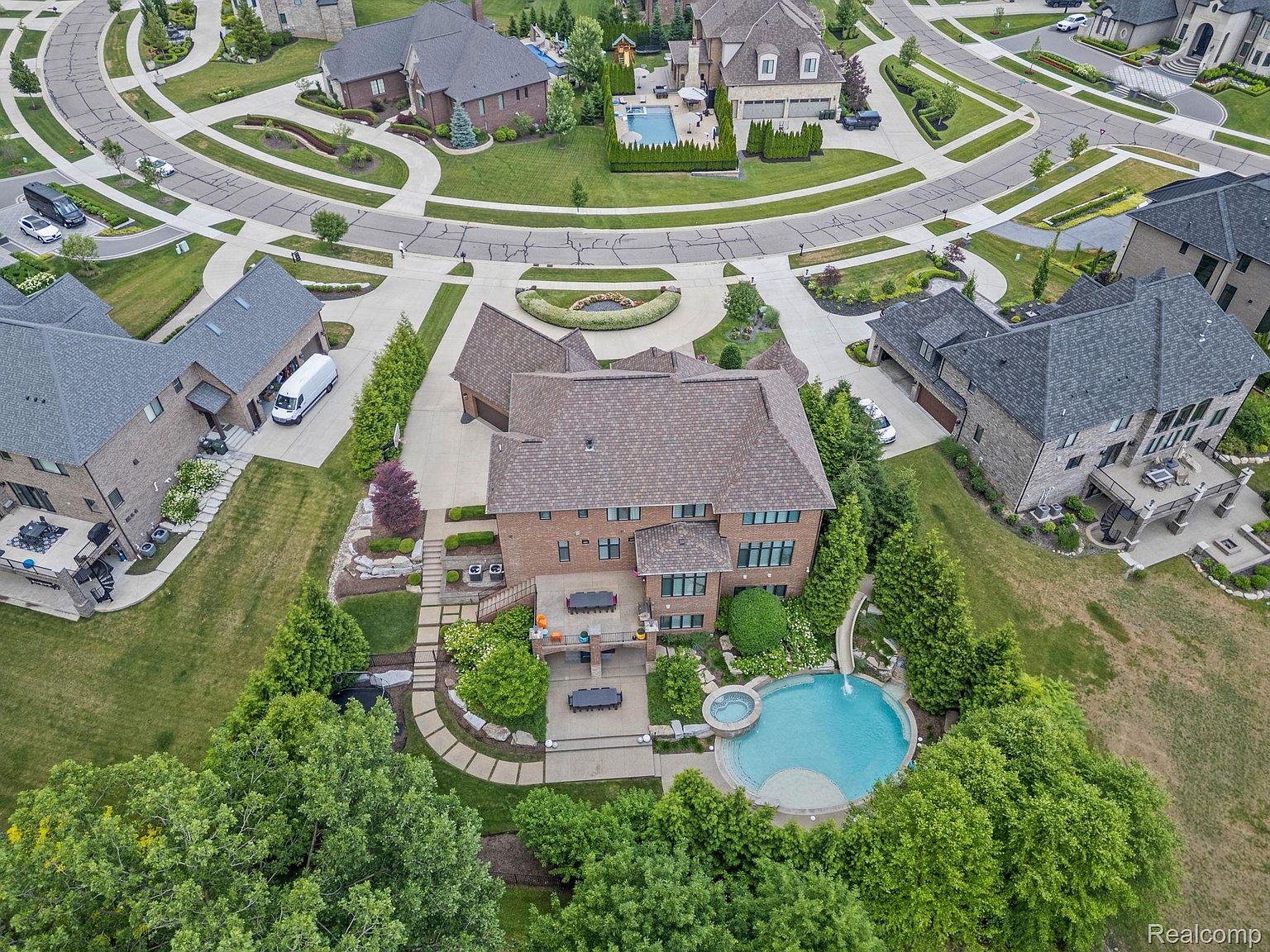 This aerial shot showcases a luxurious residential property nestled within a well-manicured neighborhood. The house features a brick exterior, a sprawling backyard with a pool and spa, and a meticulously landscaped garden. The surrounding streets are neatly arranged with lush greenery, creating an overall impression of upscale suburban living.