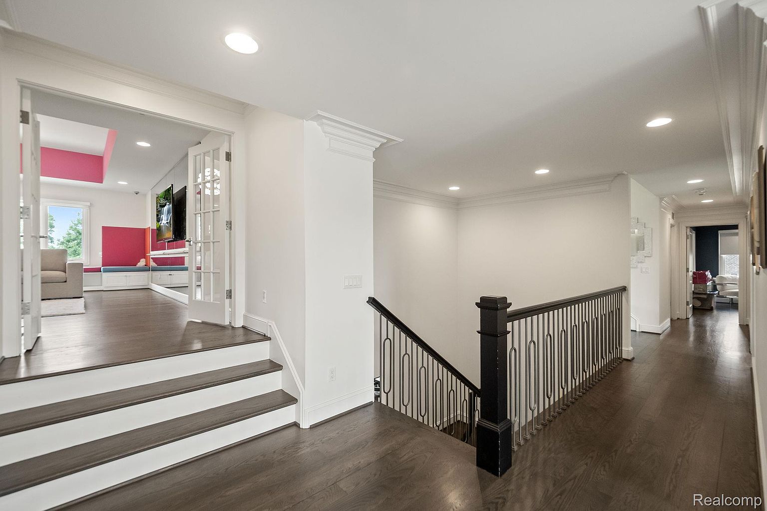 This interior shot showcases a well-lit hallway and staircase with dark hardwood flooring and white trim. The staircase features a black metal railing, and the hallway leads to other rooms, suggesting a spacious and connected layout. The overall impression is clean, modern, and inviting.