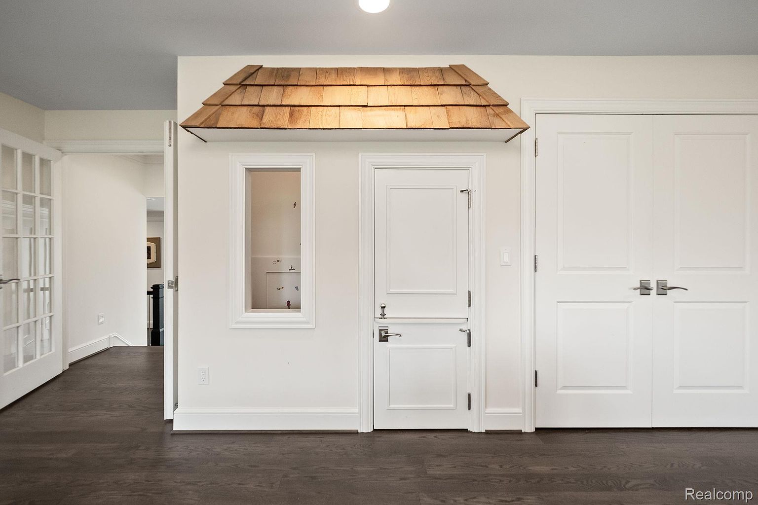 This interior shot showcases a unique hallway feature: a charming playhouse-like structure built into the wall, complete with a small window and a Dutch door. The hallway also includes a set of double doors, all painted in a crisp white that contrasts with the dark hardwood flooring. The overall impression is one of playful elegance and thoughtful design.