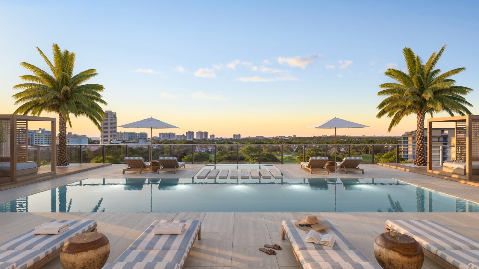 This image showcases a luxurious rooftop pool area, perfect for relaxation and enjoying the outdoors. The pool is surrounded by chaise lounges, umbrellas, and lush palm trees, creating a serene and private oasis. The expansive view of the cityscape in the background adds to the allure of this exceptional recreational space.
