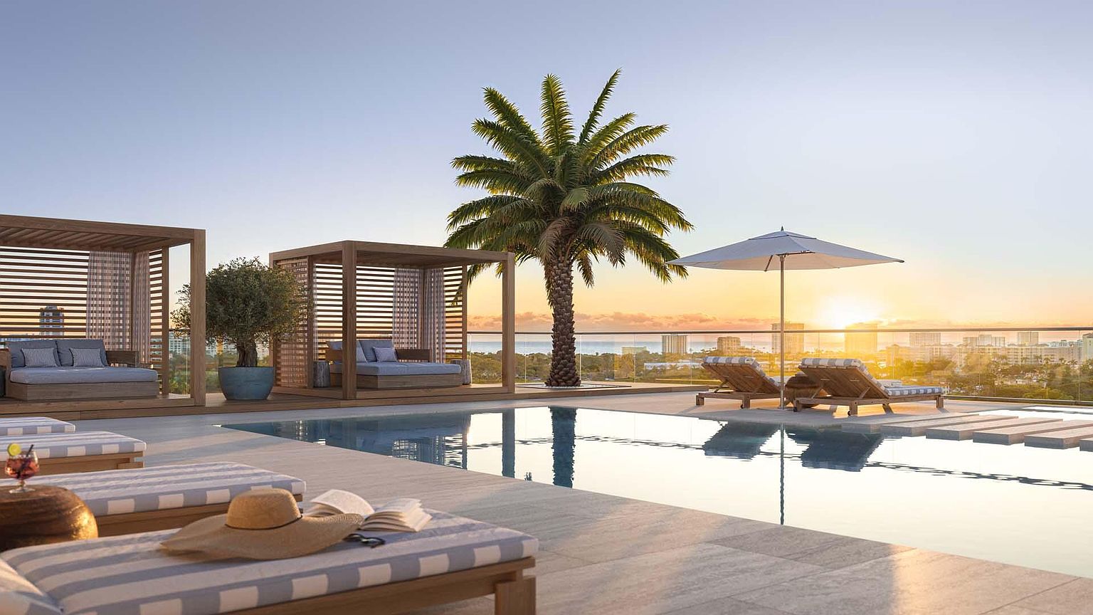 This image showcases a luxurious rooftop pool area at sunset, featuring stylish cabanas with daybeds, lounge chairs with an umbrella, and a palm tree. The pool reflects the warm light of the setting sun, and the cityscape is visible in the background, creating an inviting and upscale atmosphere. The overall impression is one of relaxation and exclusivity.