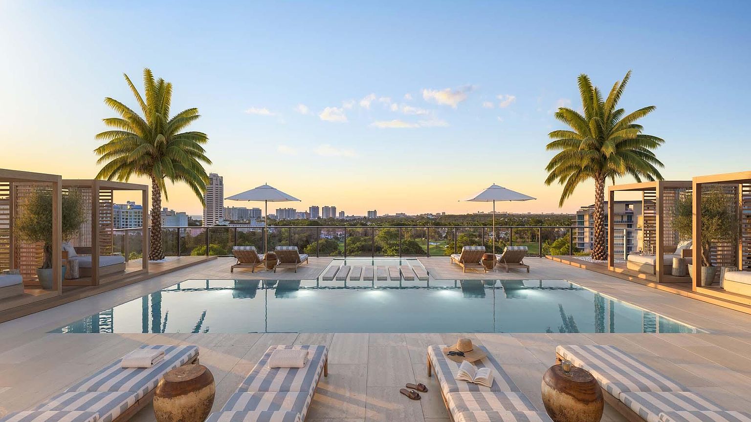 This image showcases a luxurious rooftop pool area with lounge chairs, umbrellas, and cabanas, offering a relaxing and upscale atmosphere. Palm trees add a tropical touch, while the cityscape in the background provides a stunning view. The pool's clear water invites relaxation and enjoyment.