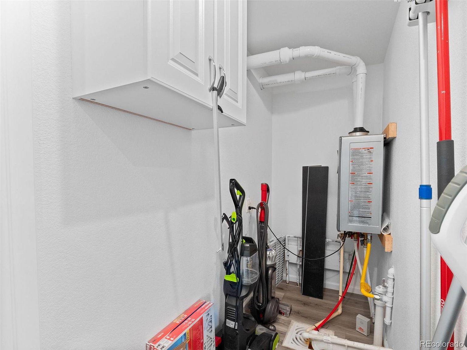 This image showcases a laundry room featuring white cabinetry and a tankless water heater. Cleaning supplies, including vacuums and mops, are neatly arranged, suggesting functionality and organization. The room's clean and uncluttered appearance enhances its appeal for potential buyers.