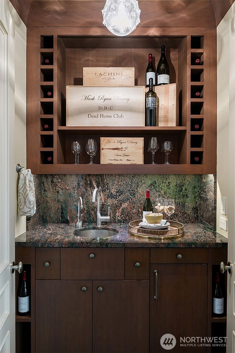 This image showcases a stylish wine cellar area, featuring dark wood cabinetry with built-in wine racks and storage. A granite countertop with a sink provides a functional space for preparing and serving wine, while wooden crates add a rustic touch. The overall design is elegant and well-suited for wine enthusiasts.
