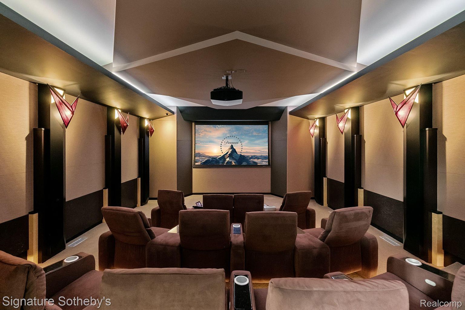 This is a luxurious home theater room featuring multiple rows of plush, reclining seating arranged in a semi-circle facing a large screen displaying the Paramount Pictures logo. The room is decorated with dark wood accents, textured walls, and unique red sconce lighting, creating a sophisticated and immersive cinematic experience. A projector is mounted on the ceiling.