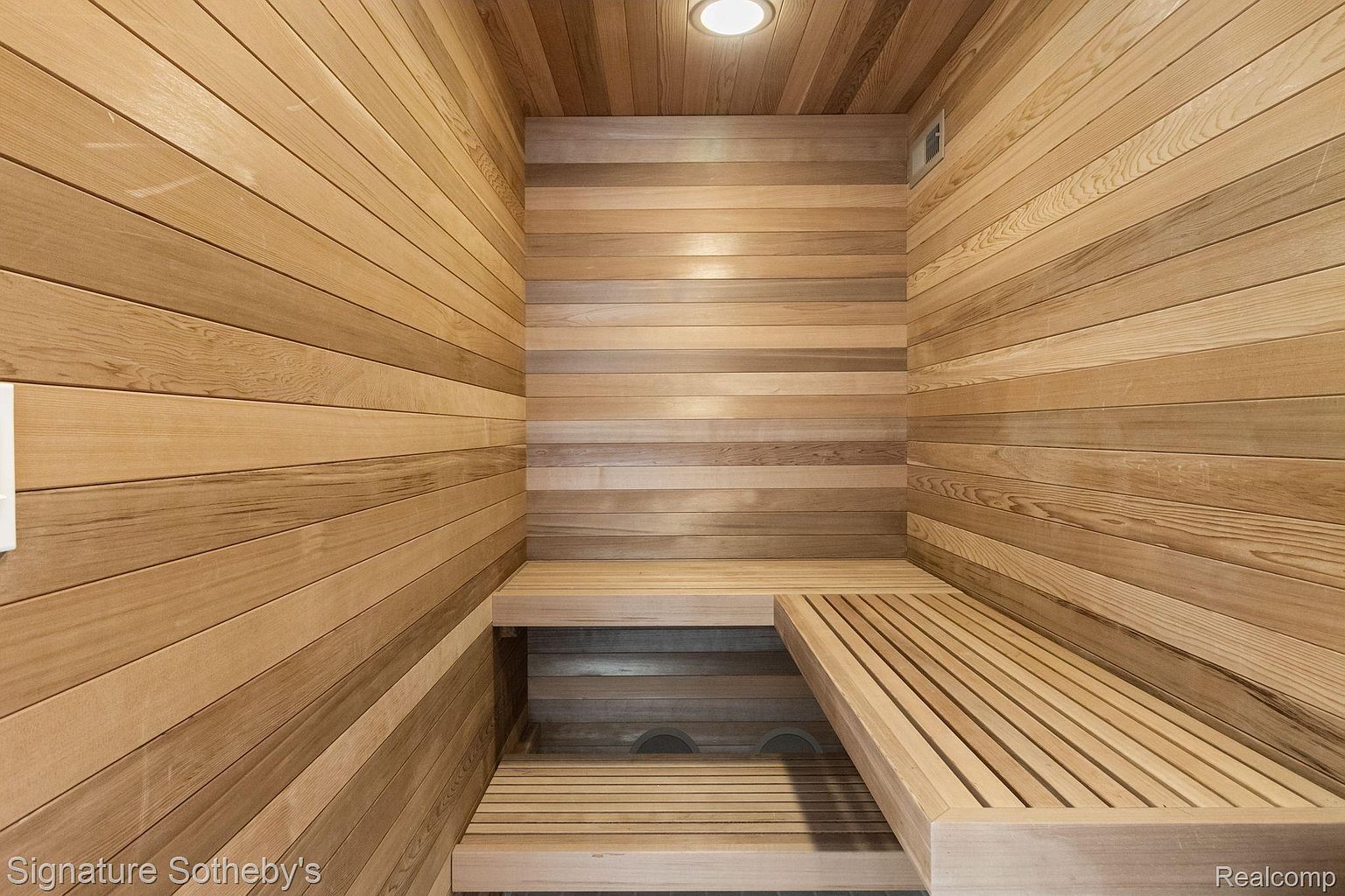 This is an interior shot of a sauna, featuring wooden walls and benches. The sauna has a clean, minimalist design with horizontal wood paneling and built-in seating. The lighting is warm and inviting, creating a relaxing atmosphere.